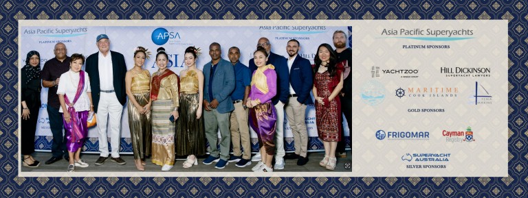 A group of people stand together, some in traditional Southeast Asian attire and others in business or casual wear, in front of a backdrop with logos for the Asia Pacific Superyachts event and sponsor names.