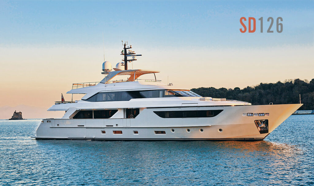 A large white luxury yacht is anchored on calm blue water near a forested shoreline at sunset. The text SD126 appears in the upper right corner of the image.