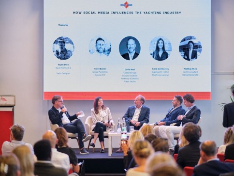 A panel of five professionals discusses on stage in front of an audience, with a screen behind them displaying their names and photos under the title How Social Media Influences the Yachting Industry.