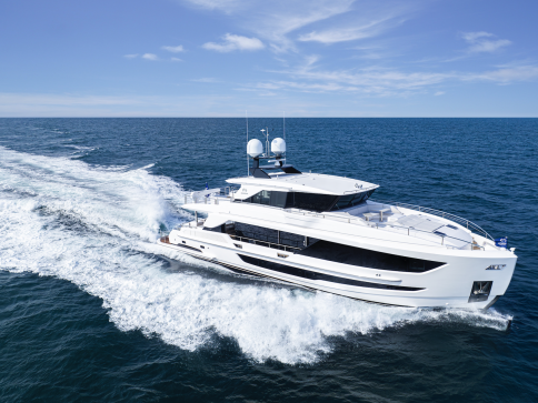 A large white luxury yacht speeds across the open sea, leaving a trail of white waves behind it under a clear blue sky.