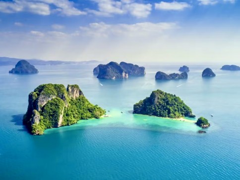 Aerial view of lush green islands surrounded by turquoise blue sea, with more distant islands and a hazy sky in the background.