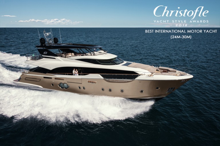 A luxury motor yacht cruises on open water under a blue sky. Text reads Christofle Yacht Style Awards 2018, Best International Motor Yacht (24m-30m). Two people stand on the yacht’s deck.