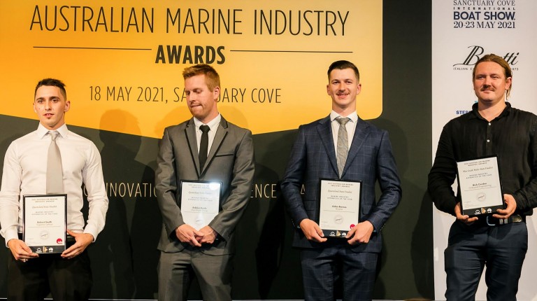 Four men in formal attire stand on stage holding award certificates at the Australian Marine Industry Awards, with event details displayed on a banner behind them.