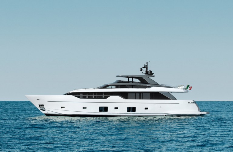 A modern white luxury yacht with black accents floats on calm blue water under a clear sky; an Italian flag is visible at the stern of the yacht.