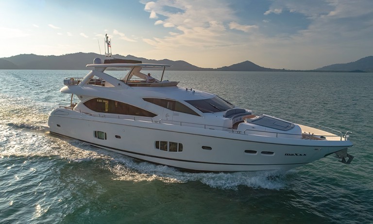 A large white luxury yacht cruises through calm blue water with hills and a clear sky in the background.