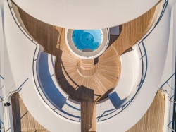 Aerial view of a luxury yacht’s curved wooden deck and stairways, centred around a circular blue jacuzzi, with sleek white railings and surfaces creating an elegant, geometric pattern.