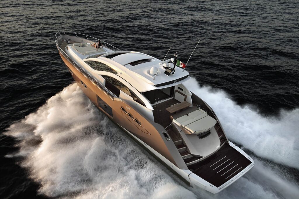 A sleek, modern yacht speeds across the open sea, creating white waves behind it. The yacht features a spacious deck, seating area, and an Italian flag at the aft.