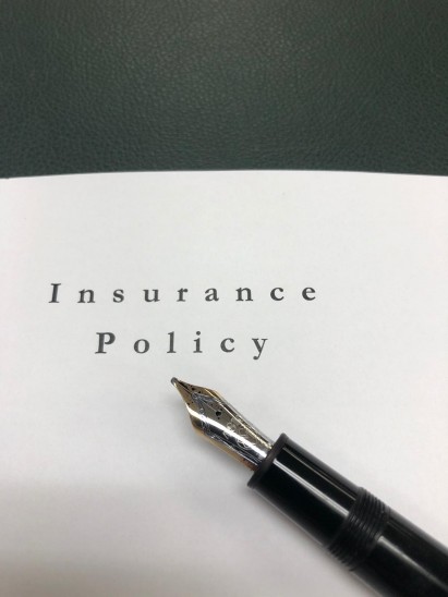 A fountain pen rests on a document titled Insurance Policy printed in black text on white paper, with a dark green surface in the background.