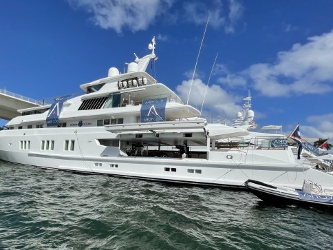 A large white yacht is moored in the water under a partly cloudy blue sky. The yacht displays multiple signs with the word AHOY on its side and has decks and aerials visible.