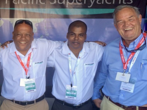 Three men wearing white shirts and exhibitor badges stand side by side, smiling at the camera in front of a sign that reads Pacific Superyachts.