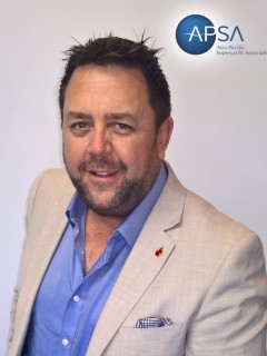 A man with short dark hair and a trimmed beard is wearing a light beige blazer over a blue shirt, standing in front of a plain background with the APSA logo in the top right corner.