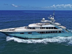 A large luxury yacht with sleek design cruises through the blue ocean under a clear sky, leaving a trail of white waves behind.