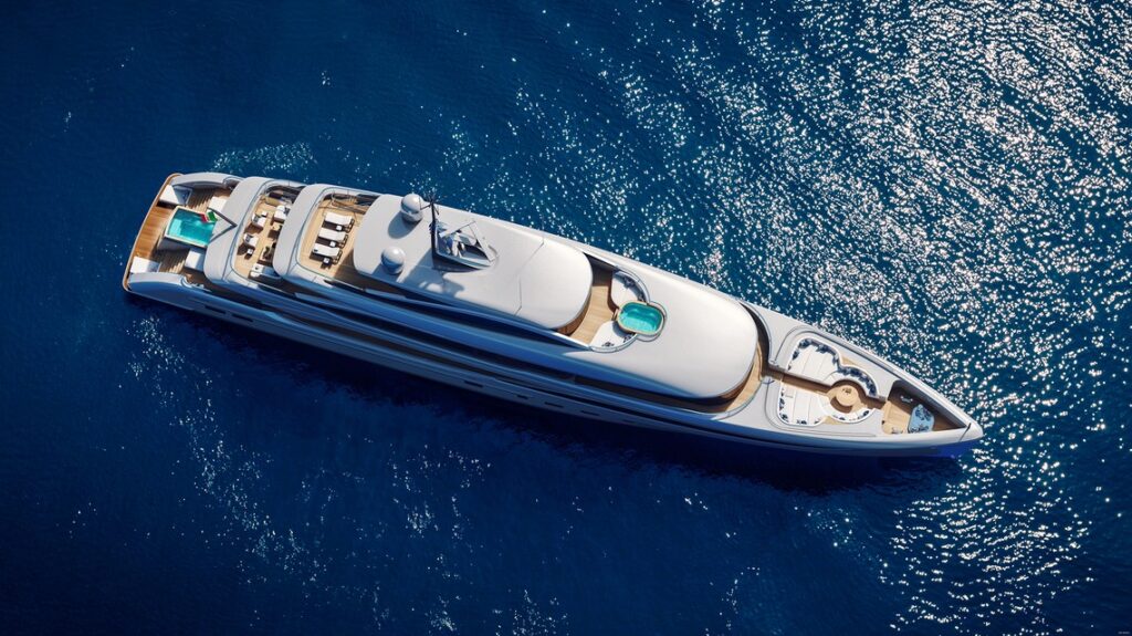 Aerial view of a large, luxurious white yacht floating on clear blue water, featuring swimming pools, sun decks, and lounging areas.
