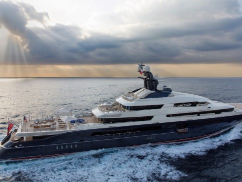 A large luxury yacht sails across the open sea under a dramatic sky with scattered clouds and sun rays streaming through, creating a serene and elegant scene.