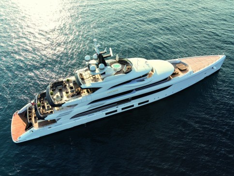 Aerial view of a large, modern white luxury yacht on calm blue water, featuring multiple decks, sunbathing areas, and sleek design elements.