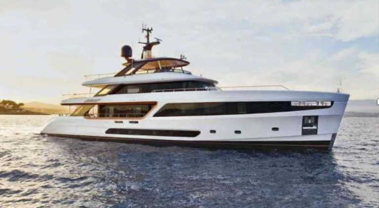 A modern white luxury yacht with sleek lines sails on calm water under a partly cloudy sky, with distant land visible on the horizon.