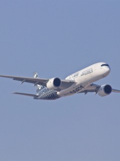 A large commercial aeroplane with Airbus A350 written on the fuselage is flying in a clear blue sky, seen from a side angle.