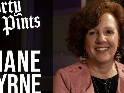 A woman with curly reddish-brown hair, wearing a pink jacket and dangling earrings, smiles at the camera. To the left, large text reads Dirty Pints and DIANE BYRNE on a dark background.