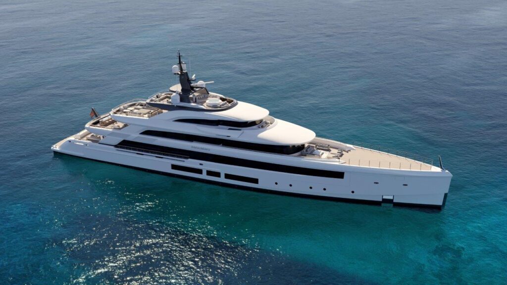 A large, modern white yacht is anchored in clear, calm blue waters. The yacht has multiple decks and sleek, contemporary design features, with sunlight reflecting off the sea around it.