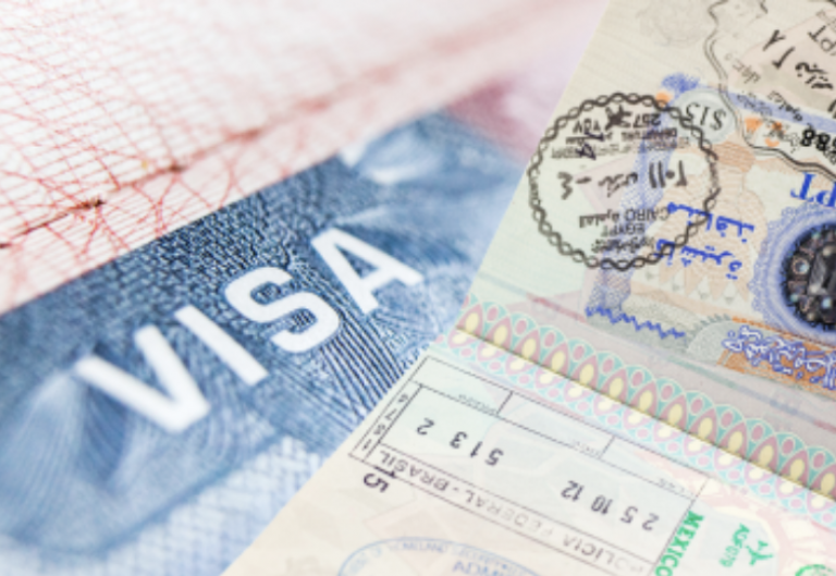 Close-up of passport pages showing a large VISA stamp and several visa stickers with official stamps and text, representing international travel and immigration documents.