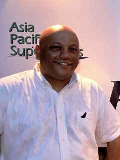 A smiling man in a white short-sleeve shirt stands in front of a backdrop with partial text that reads Asia Pacific Sup.