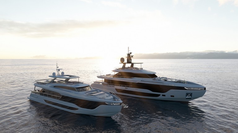 Two modern luxury yachts float side by side on calm ocean waters at sunset, with the sun low on the horizon and a distant landmass visible under a partly cloudy sky.