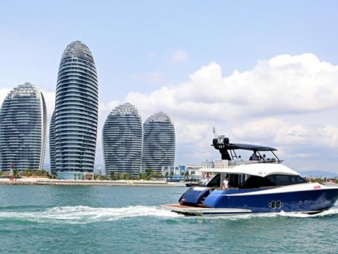 A blue and white yacht sails on the water in front of several futuristic, oval-shaped high-rise buildings under a partly cloudy sky.
