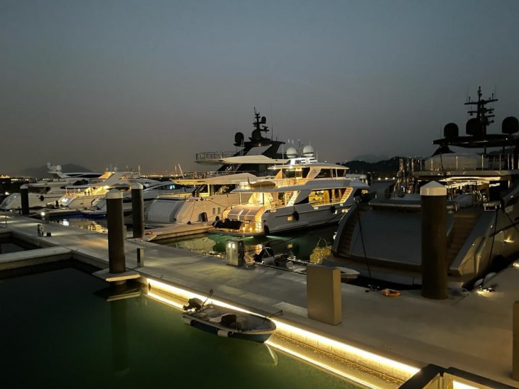 Luxury yachts moored at a marina in the evening, with soft lights illuminating the boats and pier. The sky is dim, and the water reflects the lights, creating a calm and serene atmosphere.