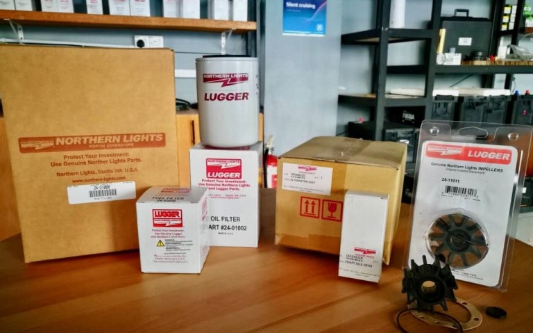 Several Northern Lights and Lugger branded engine parts, including oil filters, an impeller kit, and boxes with product labels, are displayed on a wooden table in a workshop or parts shop.