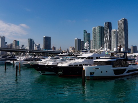 Luxury yachts moored in a marina with tall modern skyscrapers and a bridge in the background, under a clear blue sky.