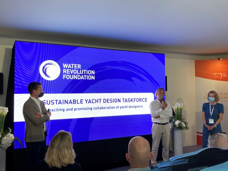 Three people stand on stage in front of a large screen displaying Water Revolution Foundation: Sustainable Yacht Design Taskforce. The audience watches as one person speaks, whilst the others listen.