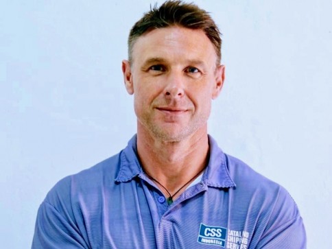 A man with short brown hair wearing a light blue polo shirt with a CSS logo stands against a plain light background, looking at the camera with a slight smile and arms folded.