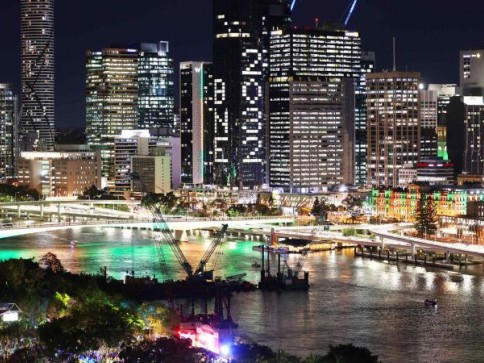 A city skyline at night with illuminated skyscrapers. One building displays 2023 in large lights. A river flows in the foreground, reflecting colourful lights from the buildings and bridges.