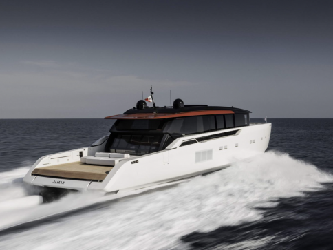 A sleek, modern white yacht with a dark-tinted cabin cruises quickly across open water, creating frothy waves behind it under a lightly clouded sky.