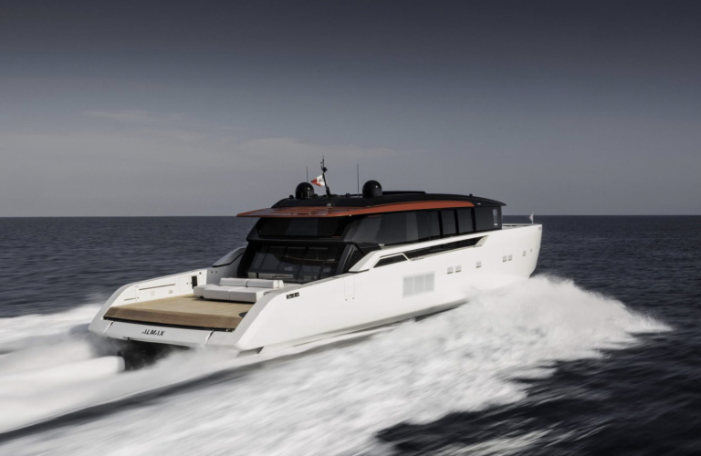 A sleek, modern white yacht with a black and red roof speeds across the open sea, leaving a trail of white waves behind it under a clear, calm sky.