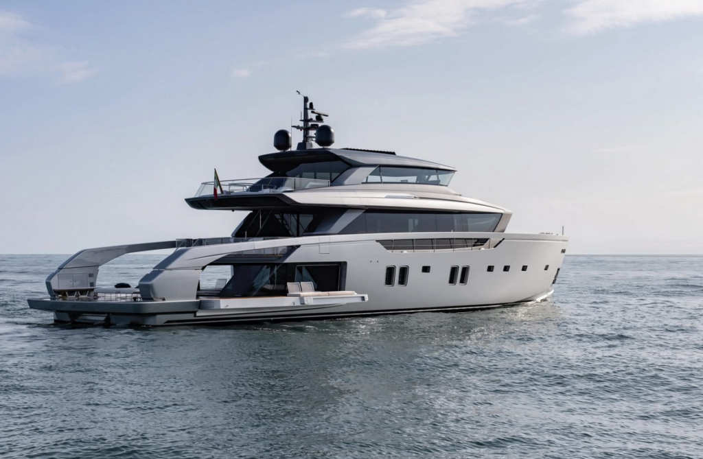 A modern white luxury yacht with multiple decks sails on calm ocean water under a partly cloudy sky.