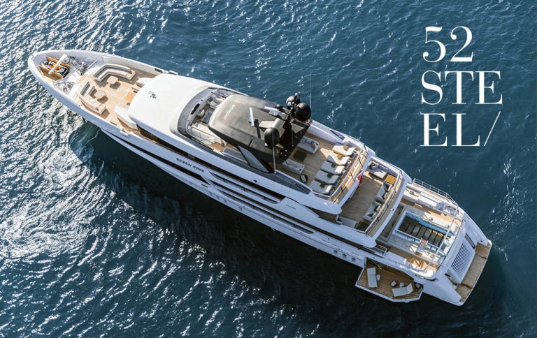 Aerial view of a luxurious white yacht named 52 Steel cruising on deep blue water, featuring multiple decks, seating areas, and a small pool at the stern. The text 52 STEEL appears on the right side of the image.