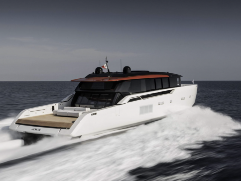 A sleek, modern white yacht with a black and red roof moves quickly across the open sea, leaving a trail of white waves behind under a cloudy sky.