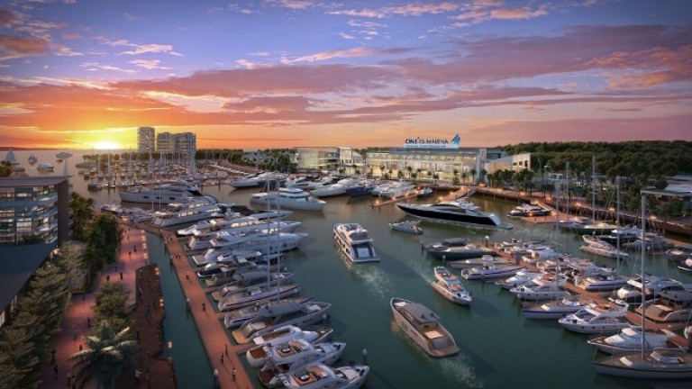 A vibrant marina at sunset, filled with numerous luxury yachts and boats moored along the waterfront, with modern buildings, lush greenery, and a golden sky in the background.
