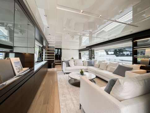 Modern yacht interior with large windows, white sofas, glass tables, and wood flooring. The space is bright with natural light, neutral décor, and elegant accents, creating a luxurious and inviting atmosphere.