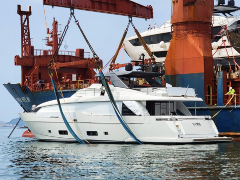 A large white yacht named Viva is being lowered into the water by cranes and straps at an industrial port, with workers and shipping equipment visible in the background.