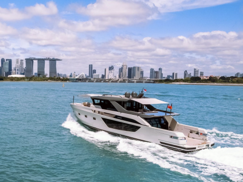 A modern white yacht sails on blue water with the Singapore city skyline, including Marina Bay Sands and the ArtScience Museum, visible under a partly cloudy sky.